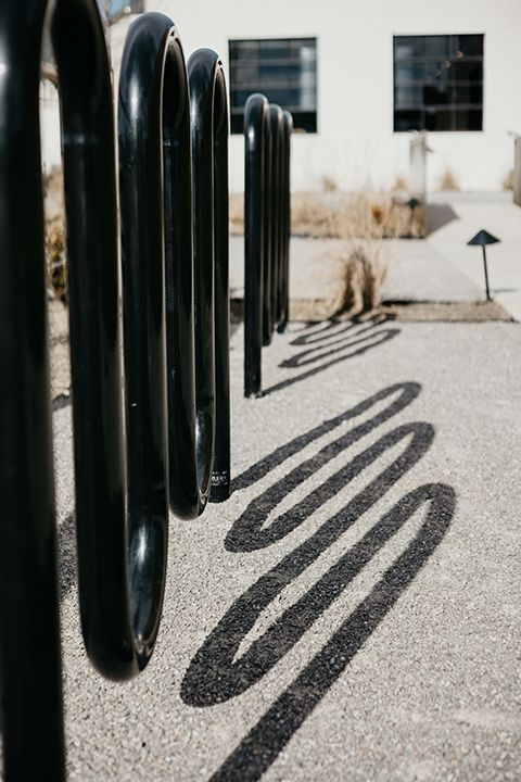 Black steel wave-style bike rack installed along a building exterior, creating high-capacity and modern bike parking for businesses.